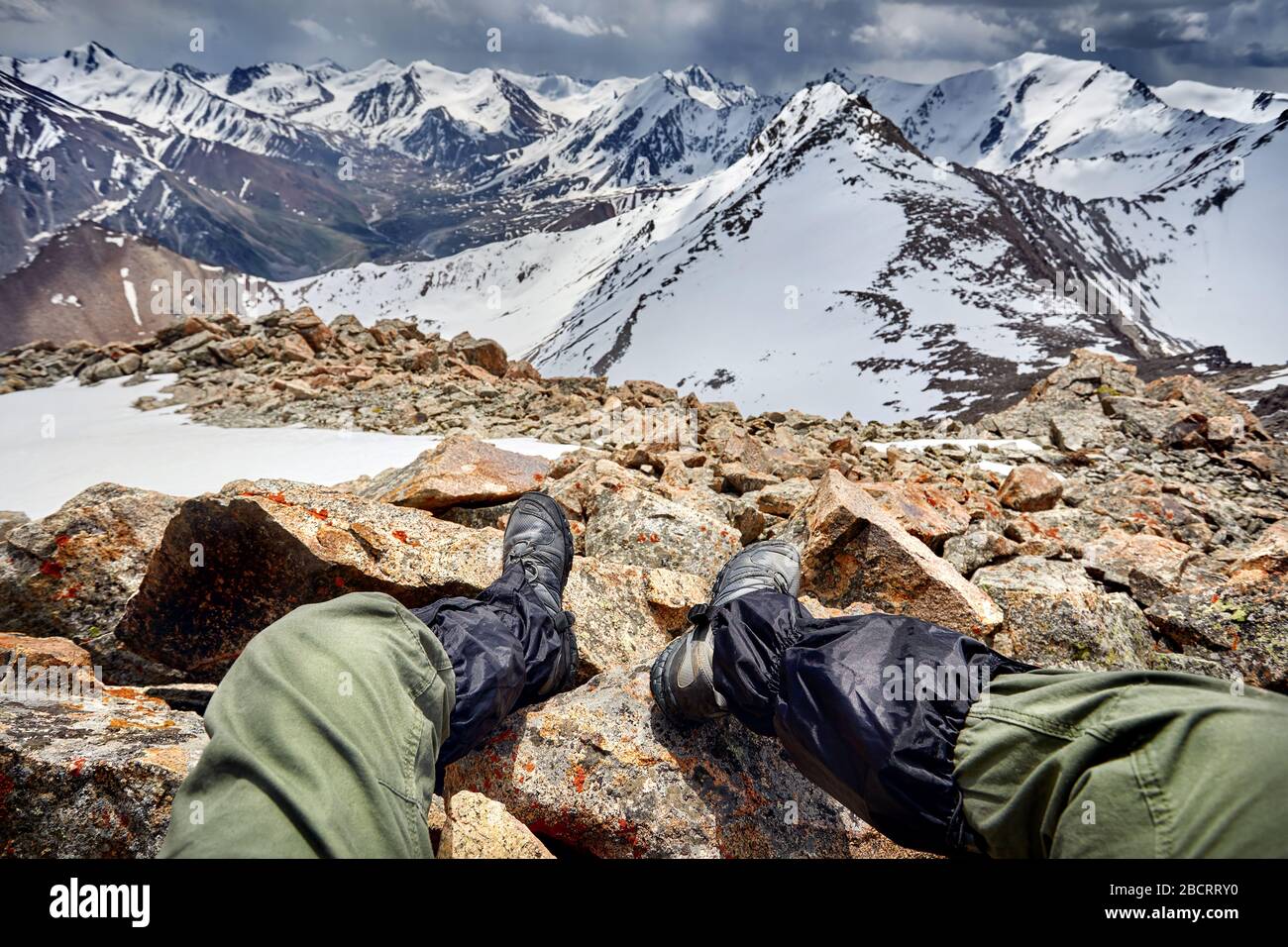 Legs of man in tracking shoes and view of Snowy Mountains with overcast stormy sky background Stock Photo