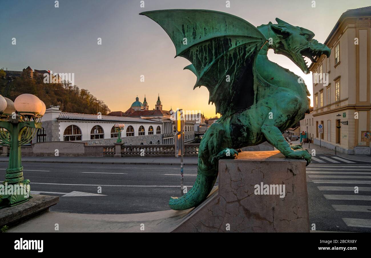 Dragon statue on Dragon bridge and Saint Nicholas Cathedral in background at sunset, Ljubljana, Slovenia Stock Photo