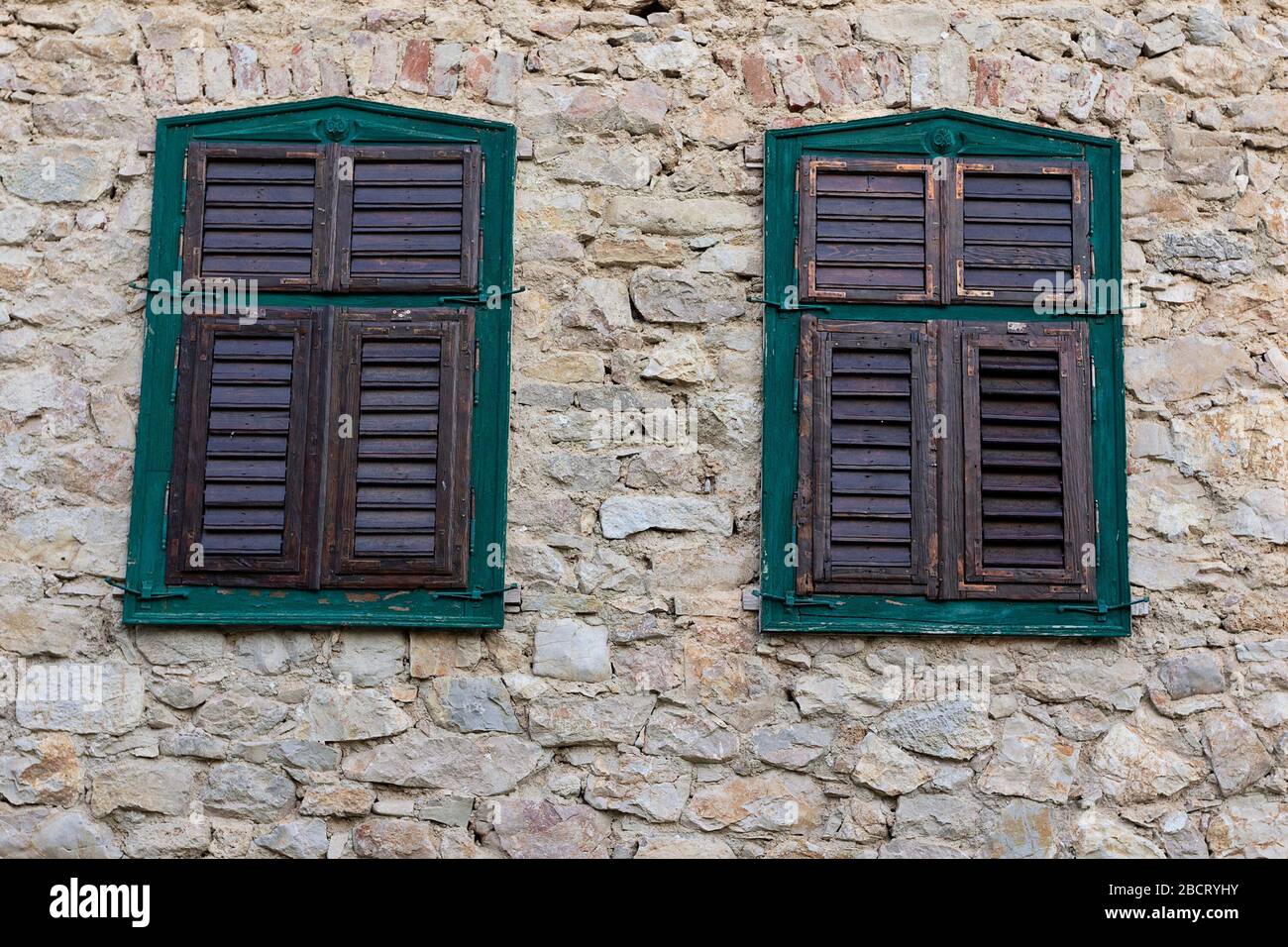 two windows on old house with stone exterior walls; wooden shutters closed Stock Photo