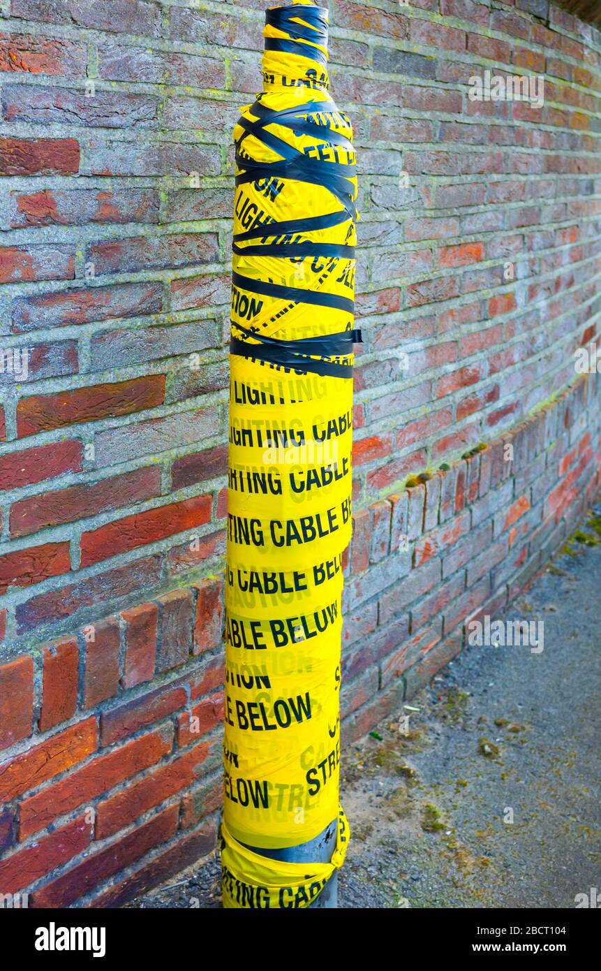 A broken lampost wrapped in black and yellow tape marked Caution Lighting Cable Below Stock Photo
