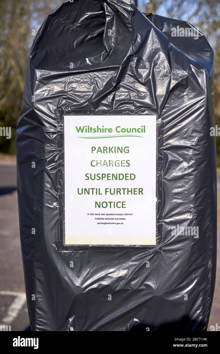 Public car park ticket machine covered with bin bag and a poster advising parking charges suspended during Coronavirus emergency Stock Photo