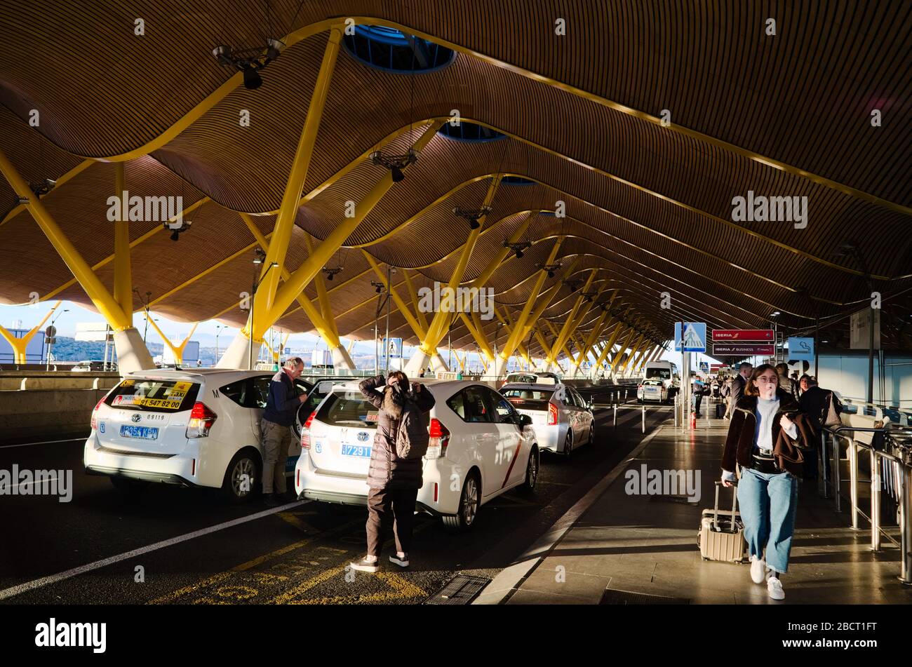 Madrid, Span - January, 2020: People arriving in taxi car on drop off parking and going with luggage to the Madrid Barajas International Airport. Stock Photo