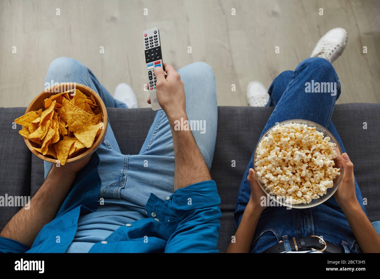 Top view close up of unrecognizable couple watching TV together while sitting on cozy sofa at home and enjoying snacks, copy space Stock Photo