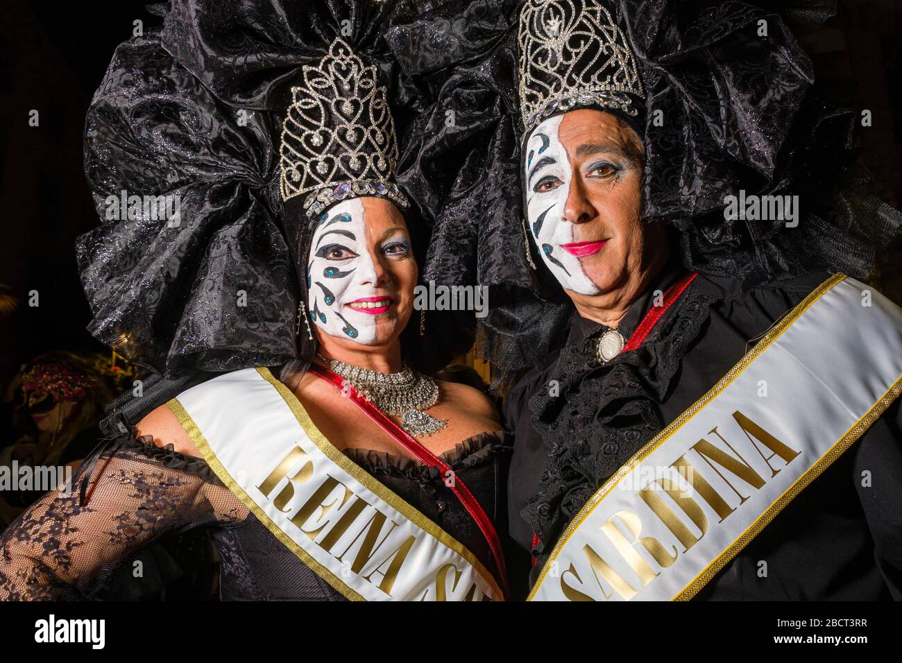 A man and a woman, dressed up as carnival queens and smiling, partying in the streets during the funeral procession Burial of the Sardine Stock Photo