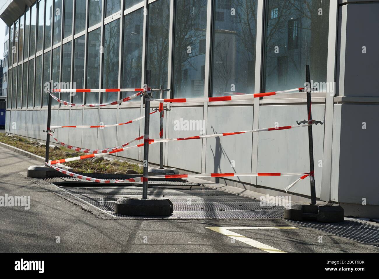 Ventilation shaft or air outlet on the street with a metal grid bordered by red and white barrier tape beside an industrial building. The shaft defect. Stock Photo