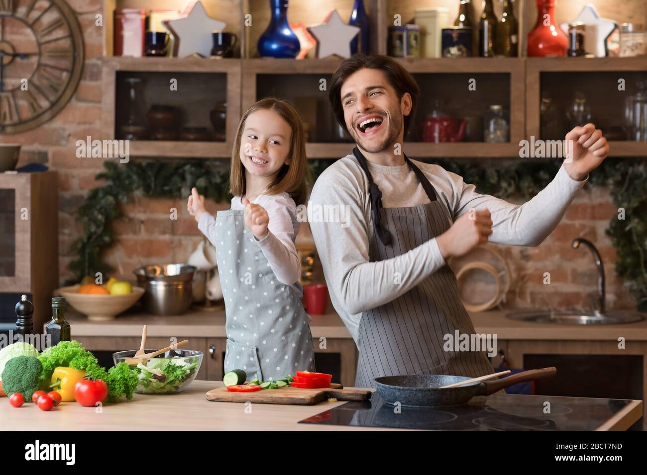 Portrait Of Cheerful Little Girl And Her Dad Dancing In Kitchen Stock Photo