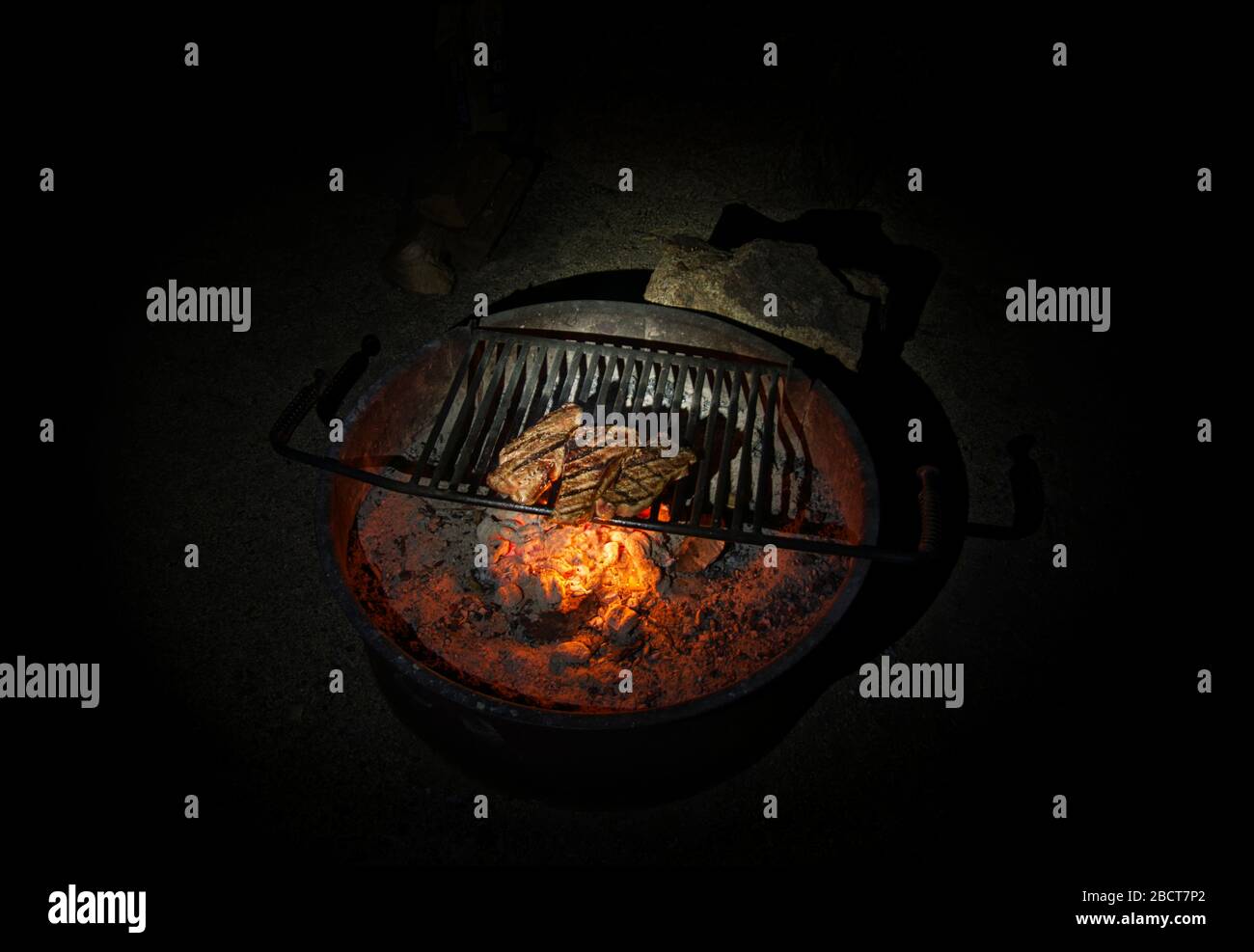 Three ready grilled steaks on a round fire bowl at the bottom Stock Photo