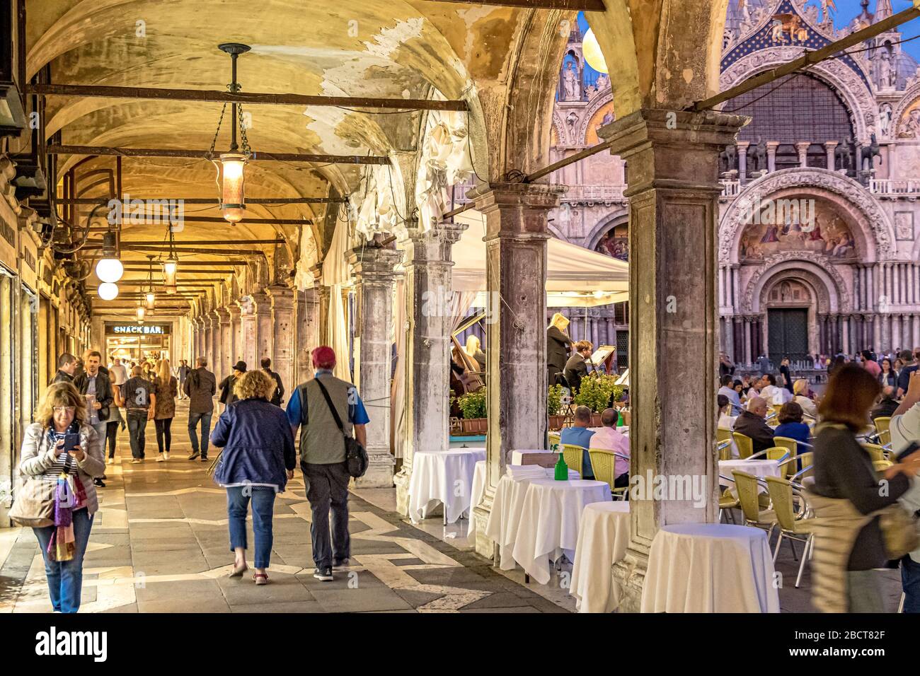People walking past Caffe Lavena enjoying an early evening stroll through the porticos and archways surrounding St Mark's Square ,Venice,Italy Stock Photo