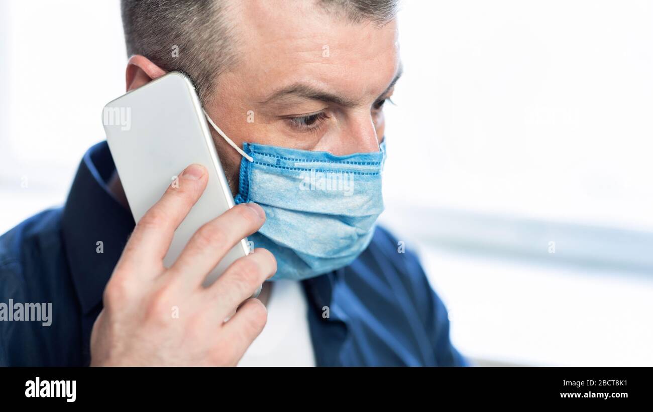 Man Talking On Phone Wearing Protective Medical Mask At Home Stock Photo