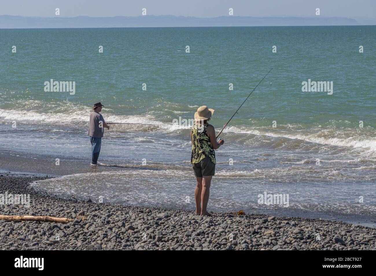 Man and woman fishing on edge of sea in Hawkes Bay, New Zealand Stock Photo