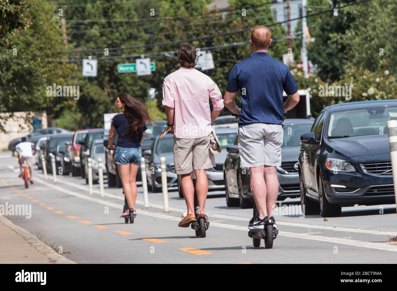 Several people on motorized scooters ride through the bike lane on a street alongside Piedmont Park on August 10, 2019 in Atlanta, GA. Stock Photo