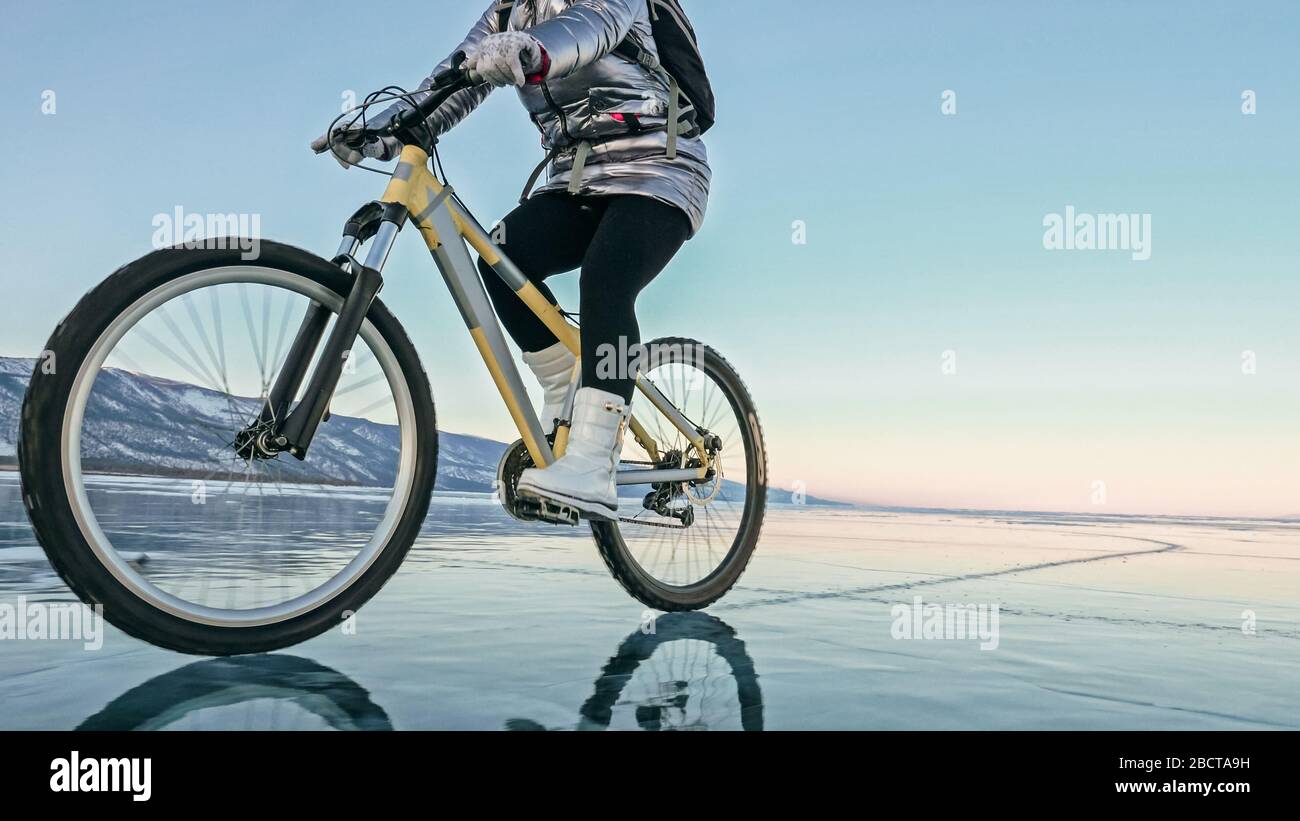 Woman is riding bicycle on the ice. Tires on bike are covered wi Stock