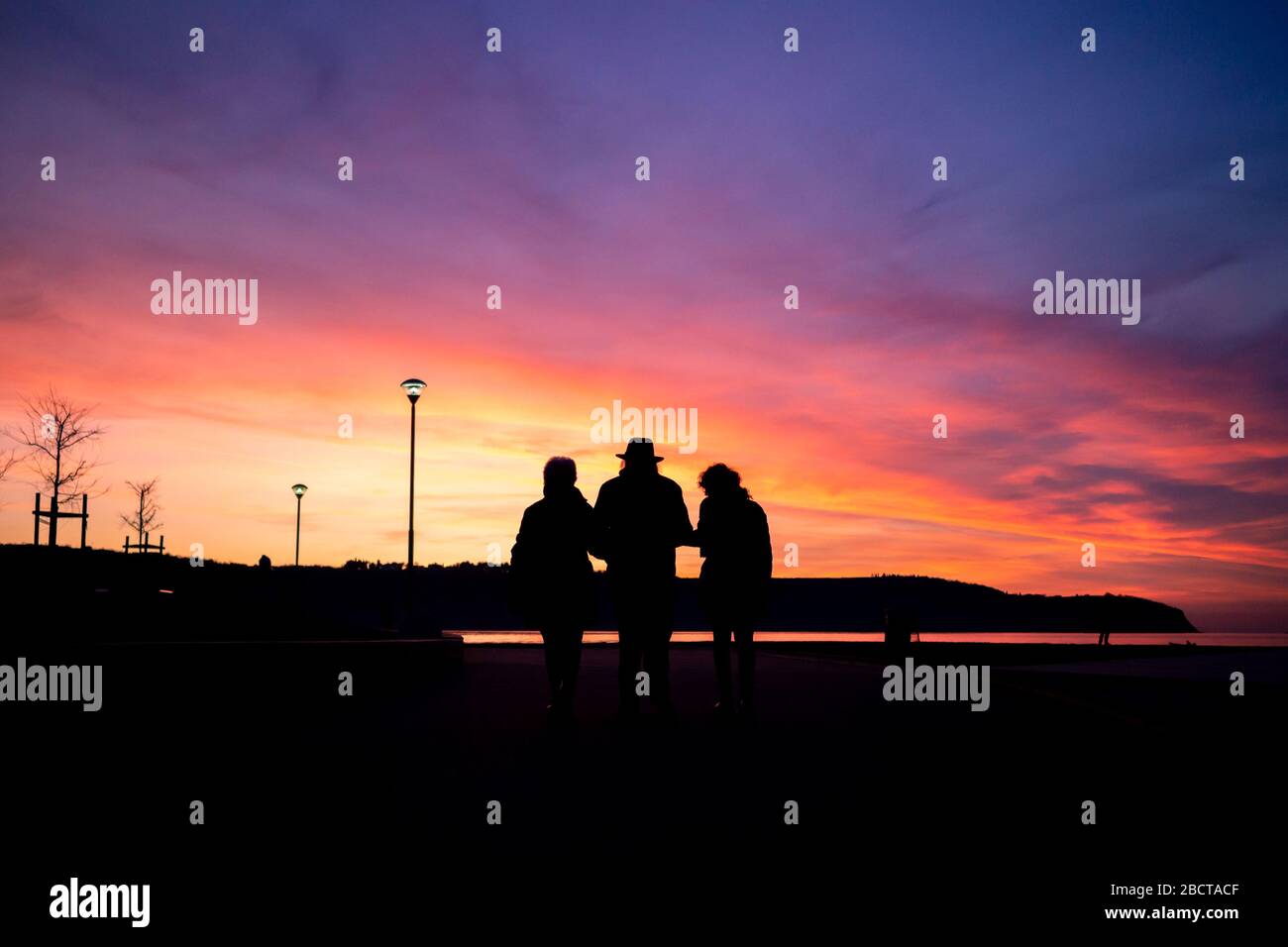 Older man with two women silhouette holding hands and walking in the sunset. Stock Photo