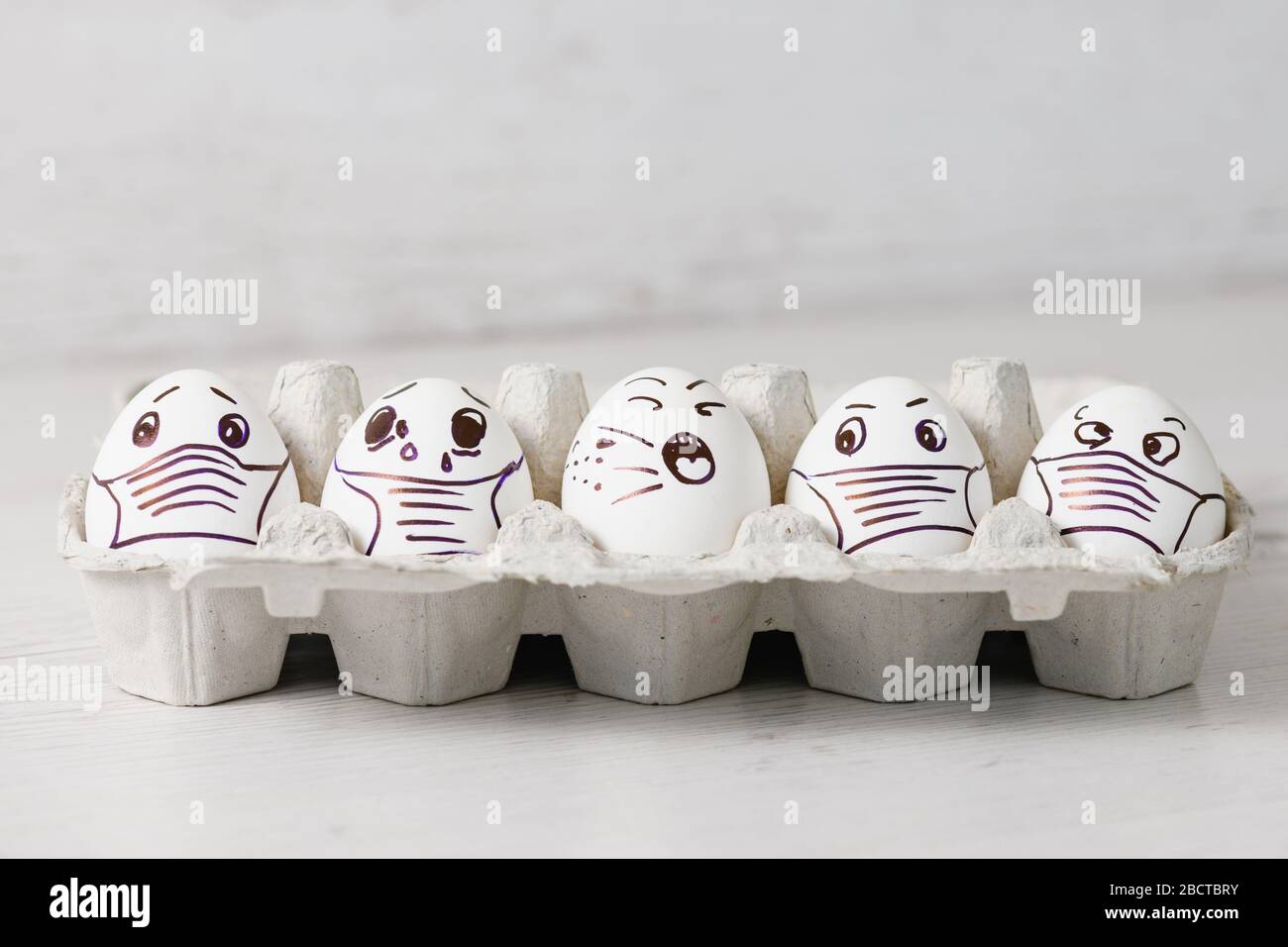 Five unhappy Easter holiday eggs in masks. Tray of white eggs with drawn funny desperate crying faces wearing medical masks at Easter holiday during c Stock Photo