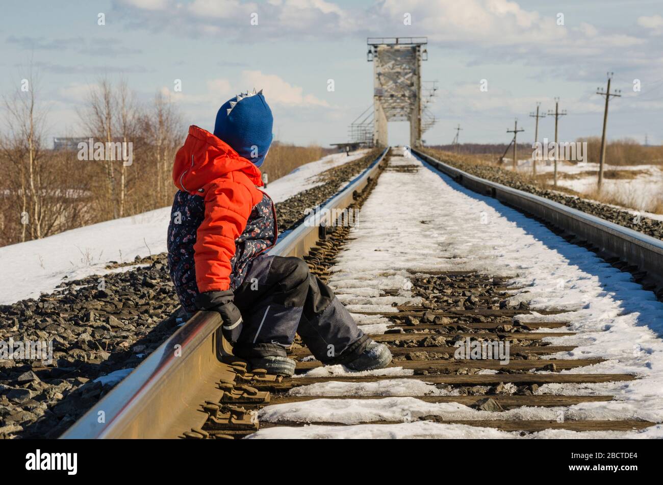 The kid is sitting on the rails of the railway. Waiting for train Stock Photo