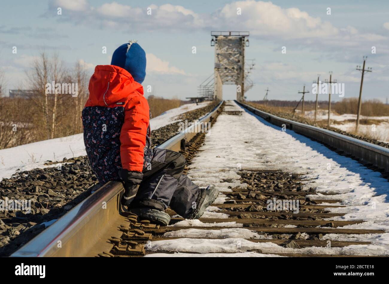 The kid is sitting on the rails of the railway. Waiting for train Stock Photo