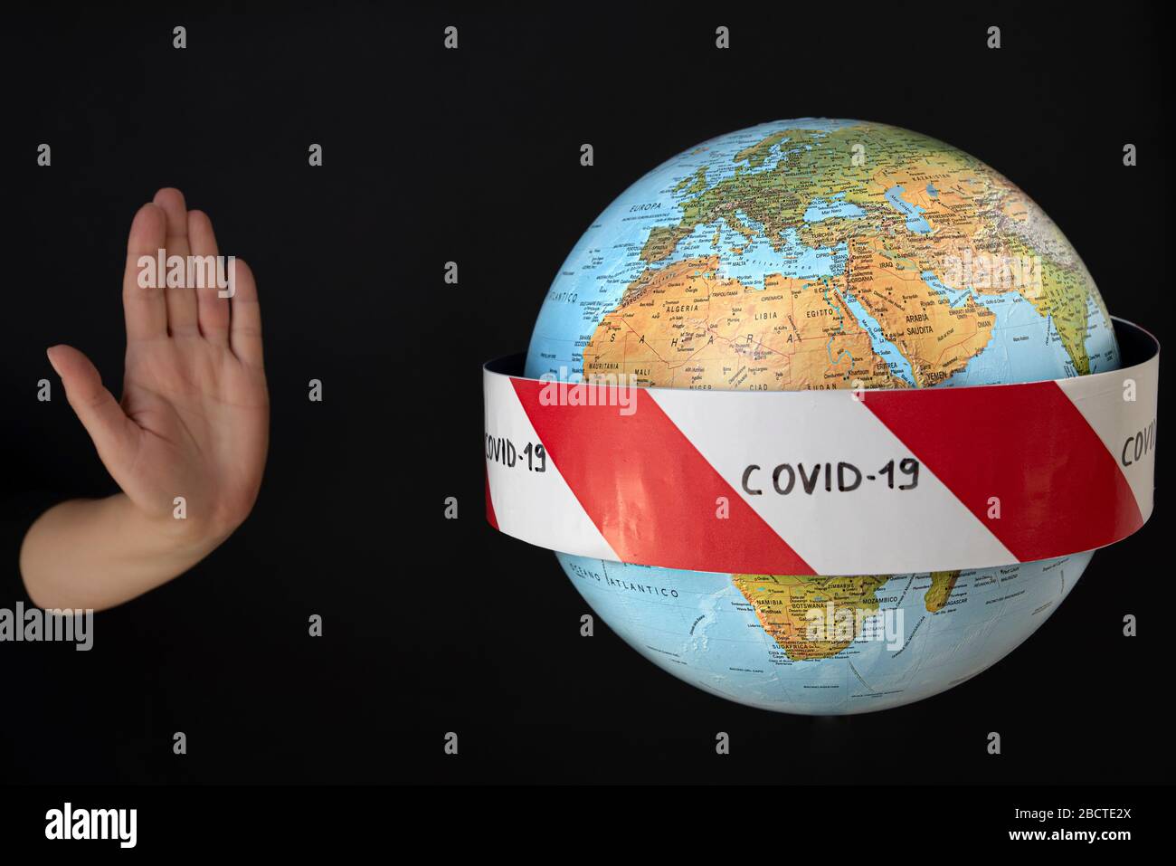 Stop the coronavirus. Hand imposes stop to spread of coronavirus, COVID-19. Planet earth with caution barrier tapes. In the foreground Europe, Africa Stock Photo