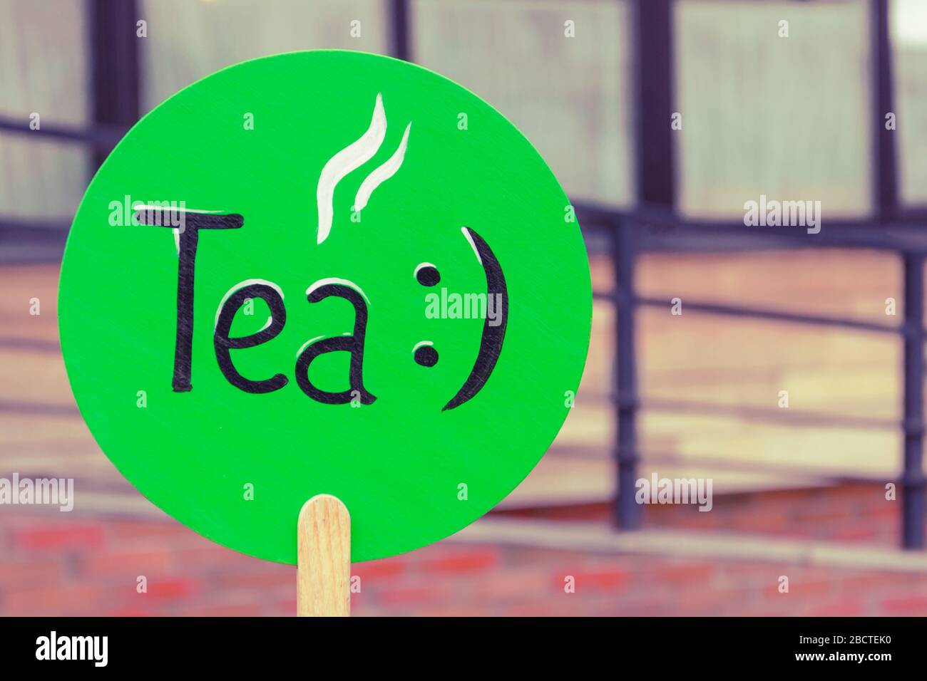 inscription tea with a smiley on a green plate of a round shape on the street. teahouse advertisement, cafe. lunch, snack, tea time Stock Photo