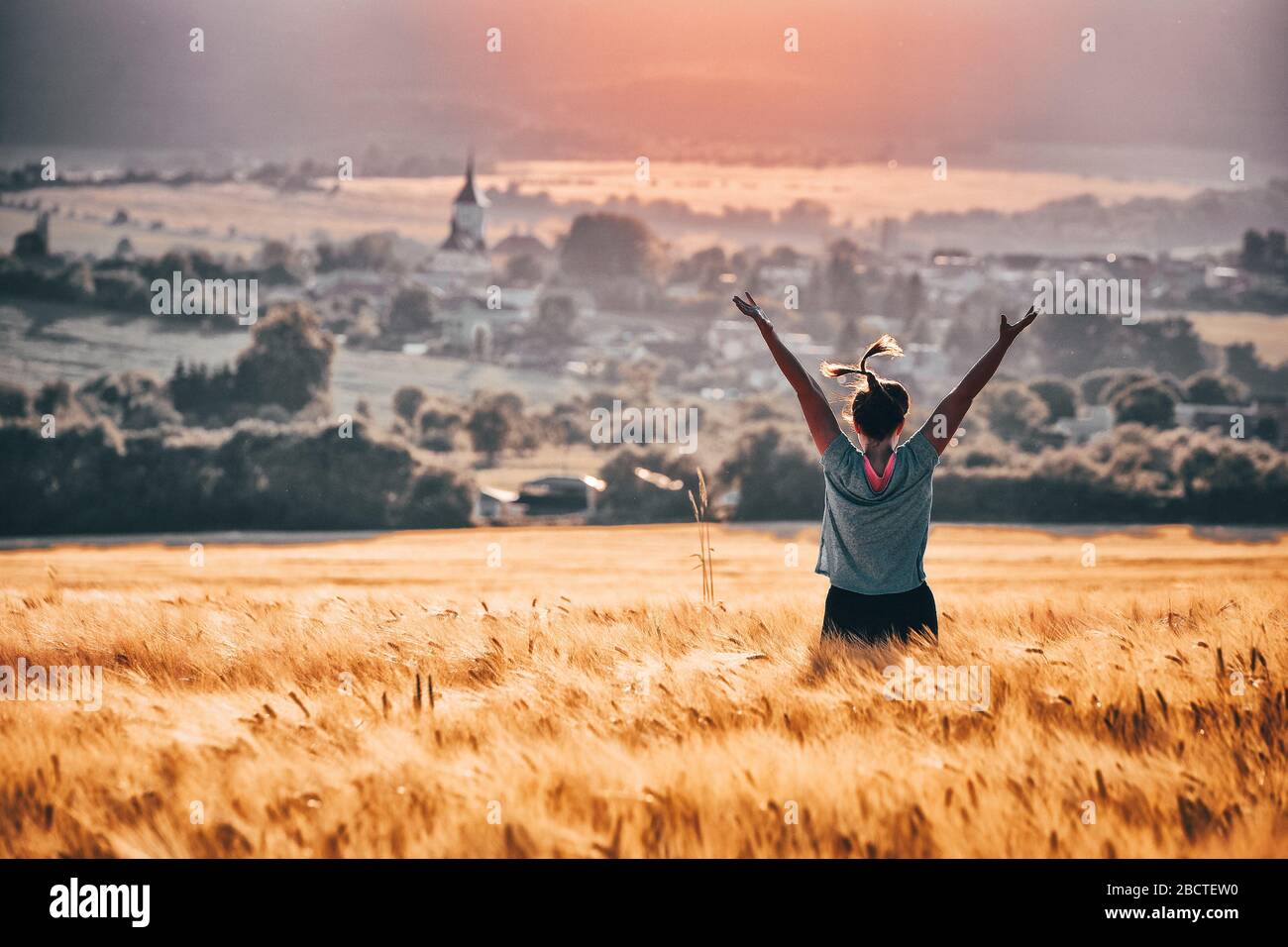 Happy young woman with open arms dancing in summer rural agricultural rye field Stock Photo