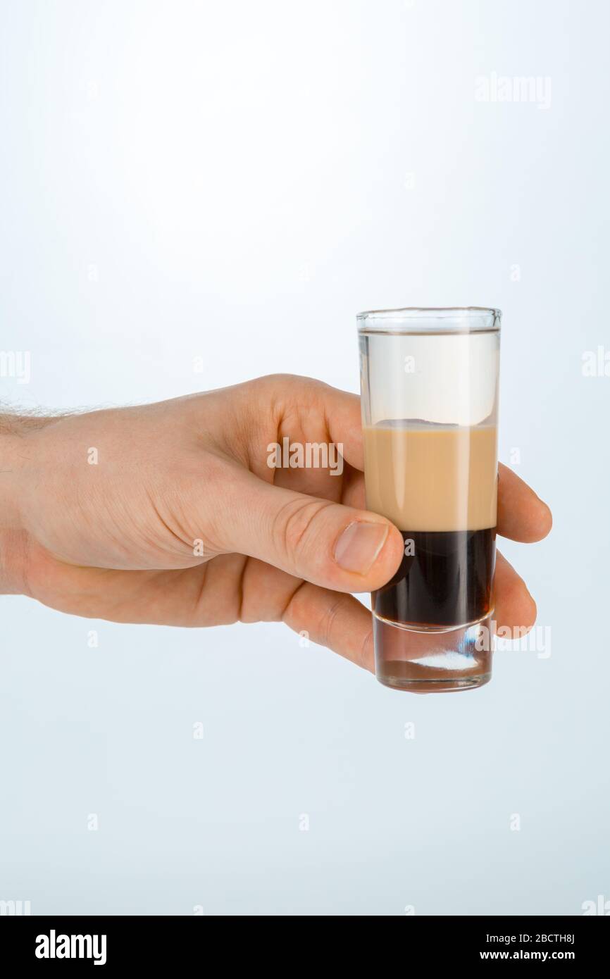 Close up of a hand holding a glass of b52 cocktail on white background with copy space. Stock Photo