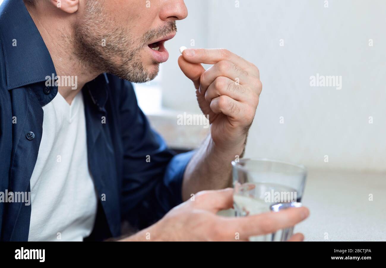 Unrecognizable Mature Man Taking Medicine Pill Sitting At Home, Cropped Stock Photo