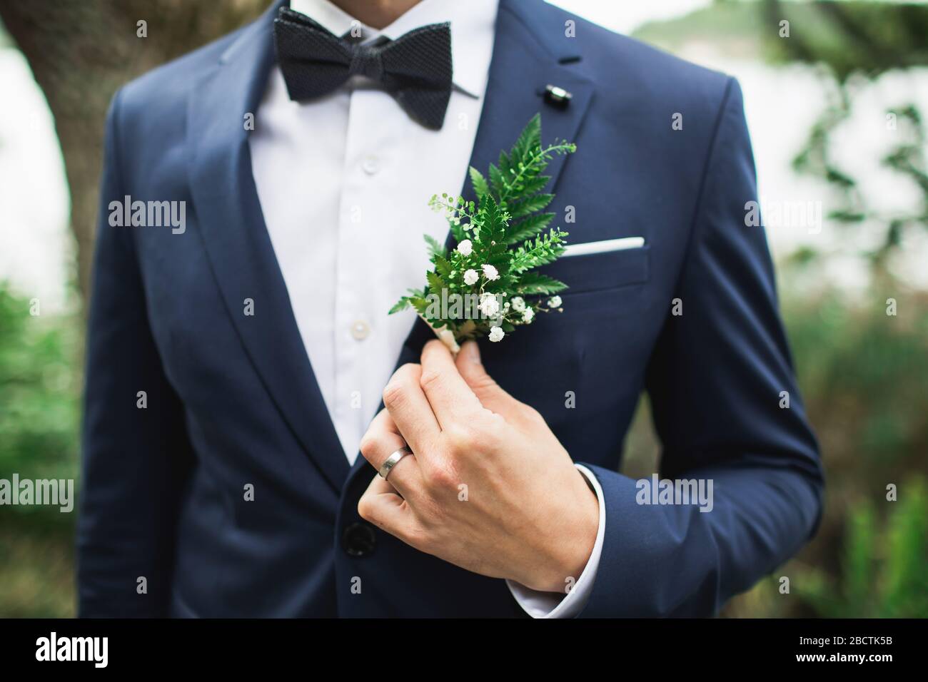 Elegant groom's boutonniere with fern and white flowers. Holding with hand. Forest style. Stock Photo