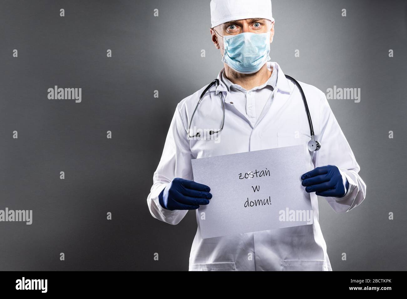 Medic doctor in white suit, protective gloves and medical mask holding card with message stay at home Stock Photo