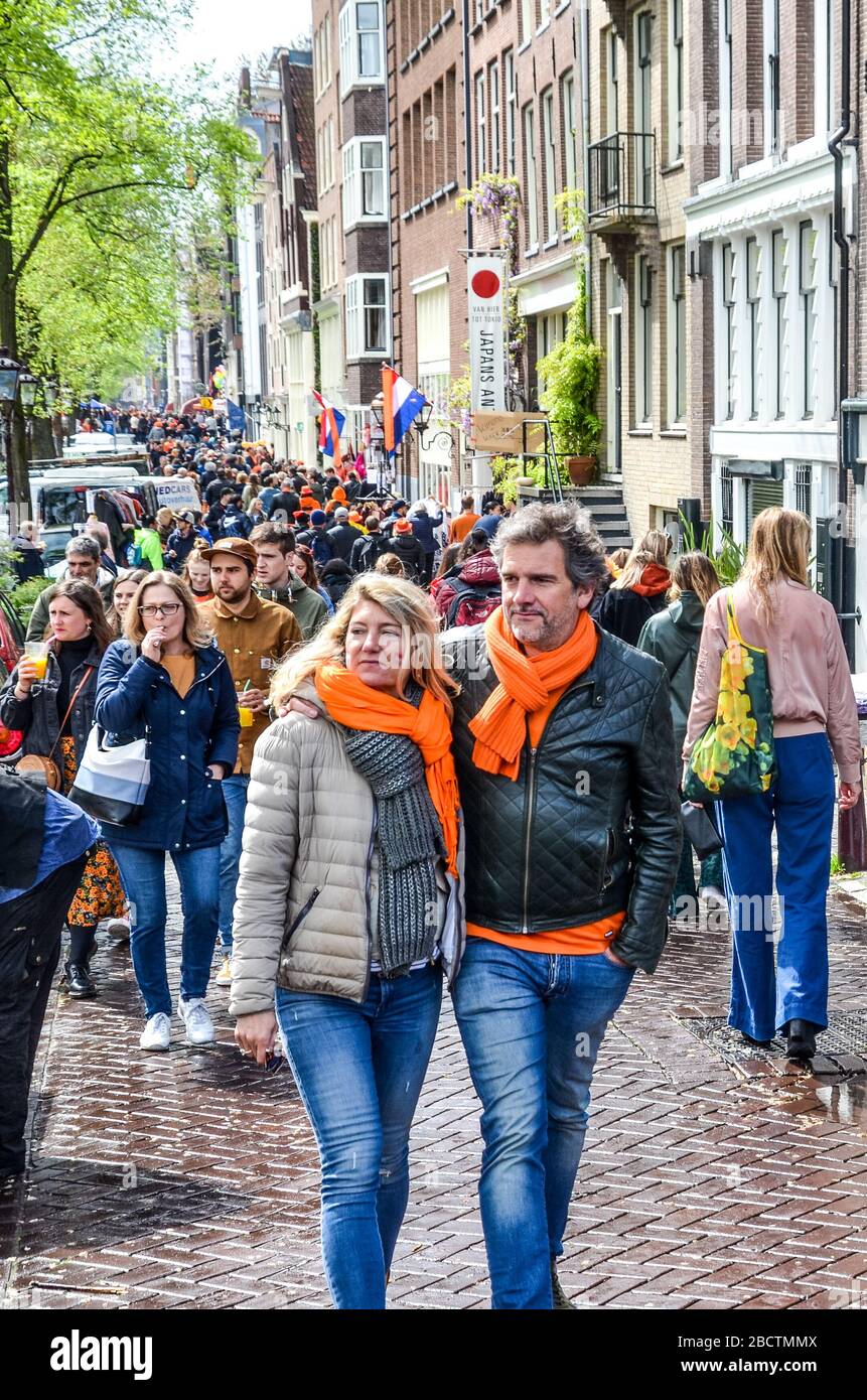 Amsterdam, Netherlands - April 27, 2019: People on the street wearing orange accessories celebrating the Kings day, Koningsdag, the birthday of the Dutch King Willem-Alexander. Overcrowded streets. Stock Photo