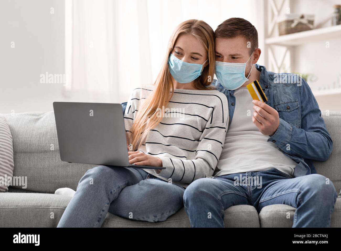 Young couple in protective masks purchasing in internet Stock Photo - Alamy