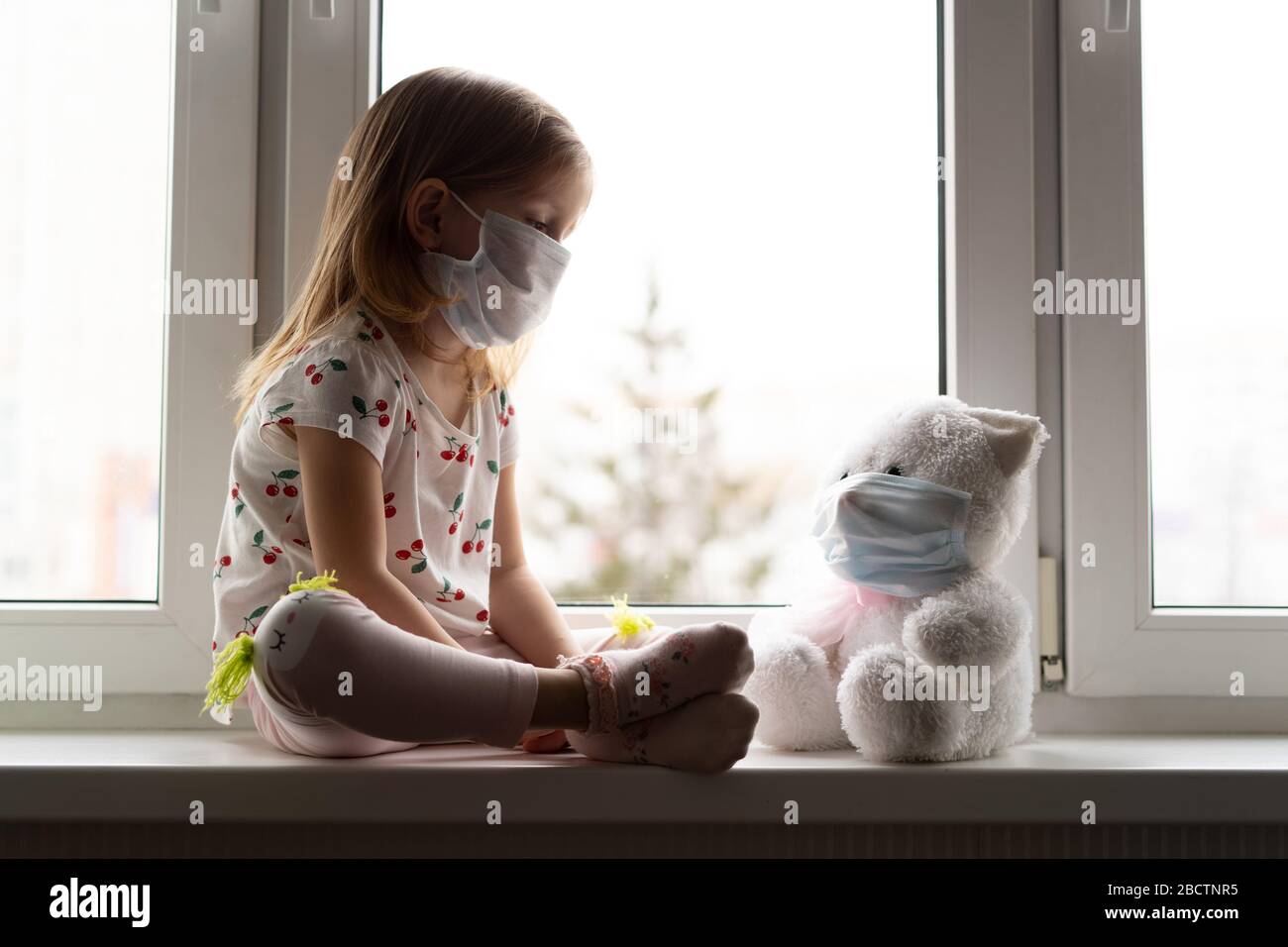 Sad child and his teddy bear both in protective medical masks. Children and illness COVID-2019 disease concept Stock Photo