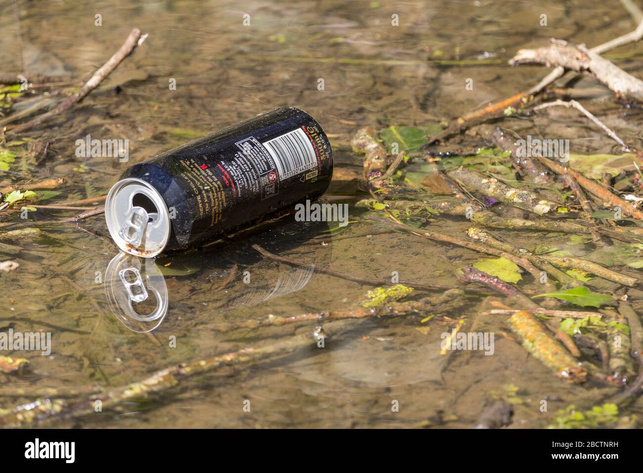 Water pollution discarded food container alumimium drinks can thrown in stream unrecycled metal product carelessley discarded by consumer Horsham UK Stock Photo