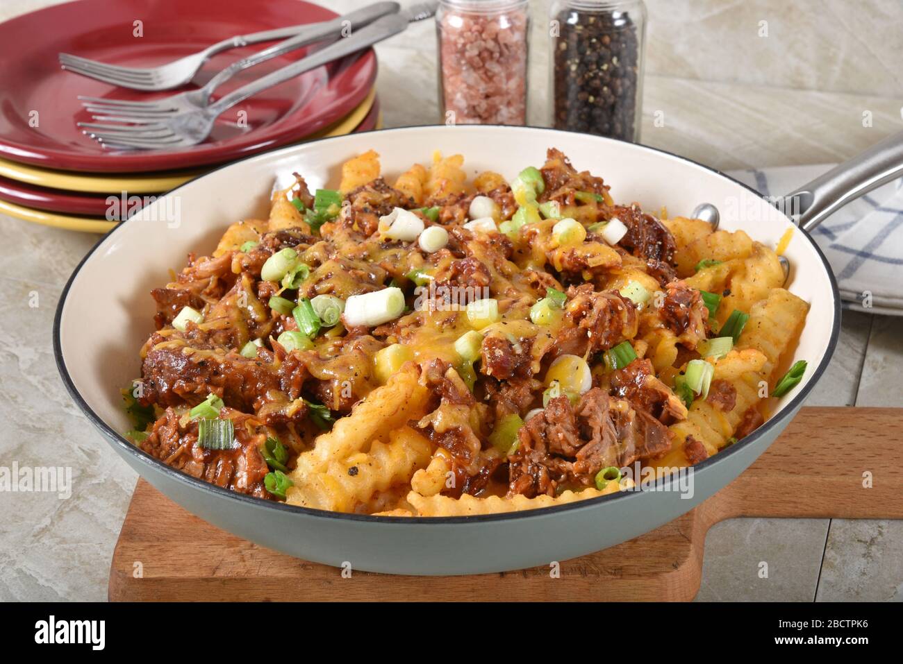 Loaded french fries with barbecues pulled pork, green onions and cheese served in a cast iron skillet Stock Photo