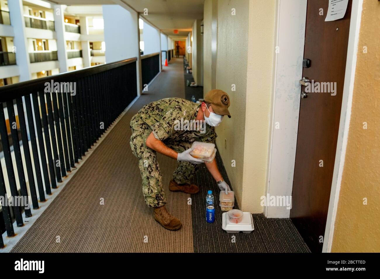 A U.S. Navy sailor delivers food to hotel rooms where sailors from the aircraft carrier USS Theodore Roosevelt who have tested negative for COVID-19 are quarantined April 3, 2020 in Tamuning, Guam. The sailors will be required to remain in quarantine for at least 14 days. Previously the ships commanding officer Capt. Brett Crozier was relieved of duty March 31, 2020 after pleading for help to stem the spread of COVID-19 cases on his ship. Stock Photo