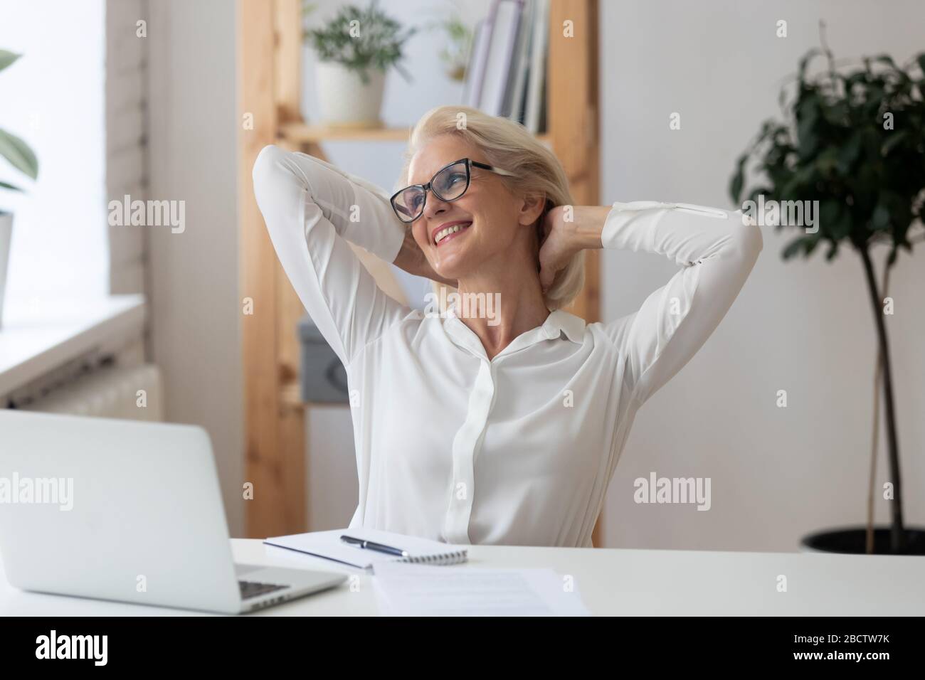 Satisfied 60 years old businesswoman with hands behind head relaxing ...