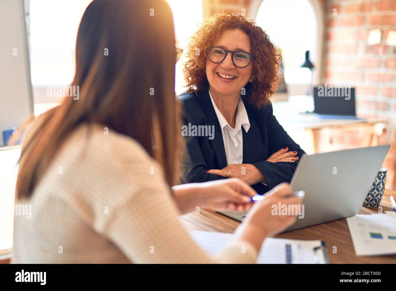 Two beautiful businesswomen smiling happy and confident. Sitting with ...