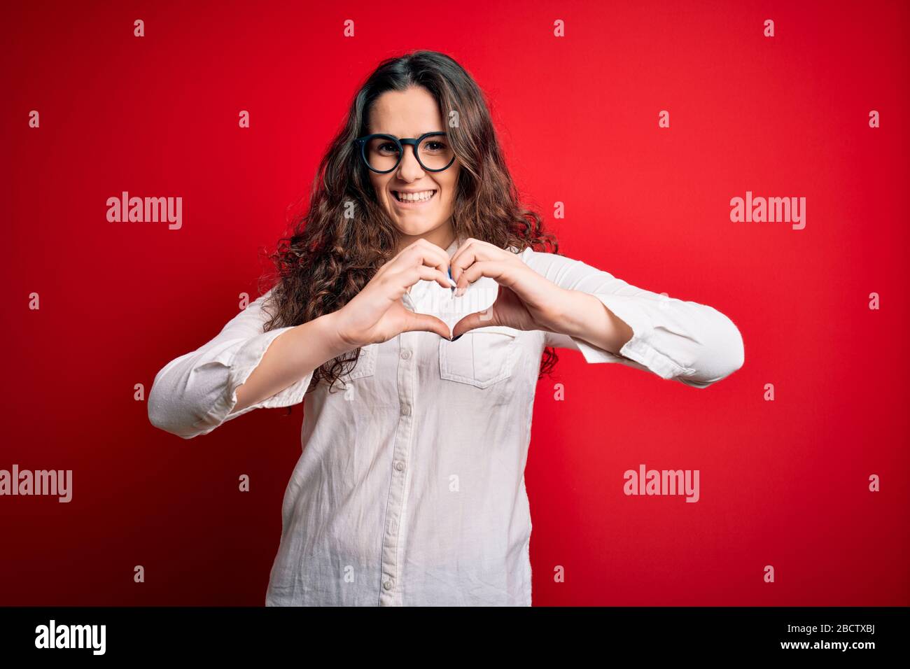 Young beautiful woman with curly hair wearing shirt and glasses over ...