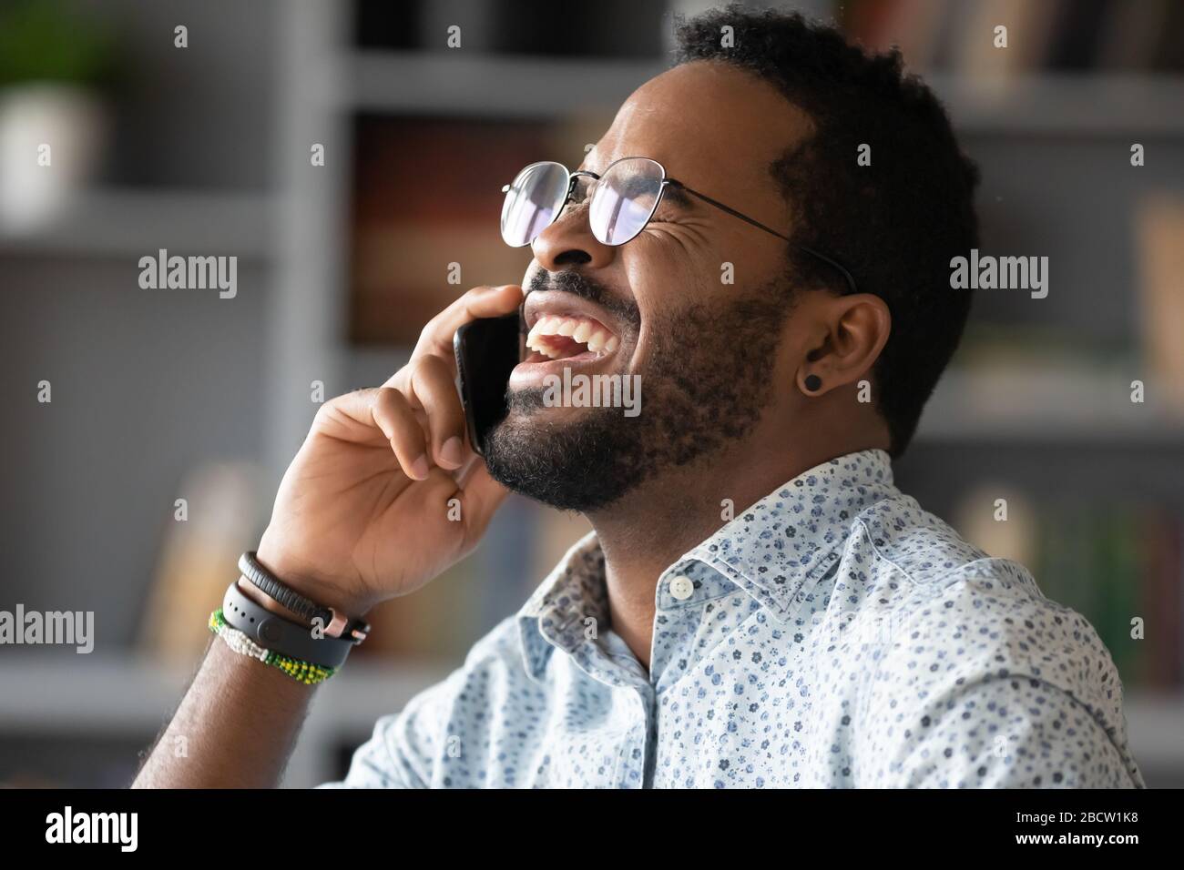 Overjoyed biracial man laugh talking on smartphone Stock Photo