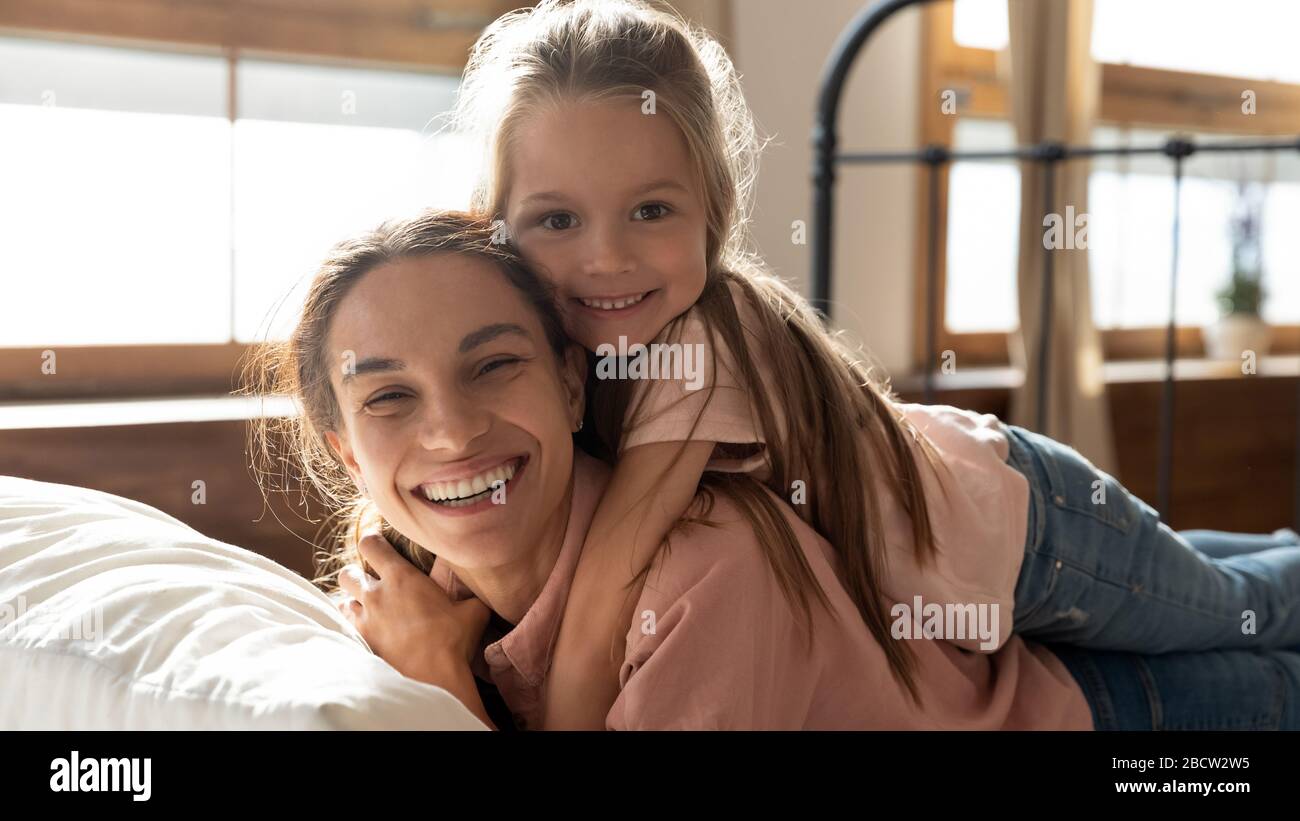 Happy woman lying on bed with daughter on back. Stock Photo