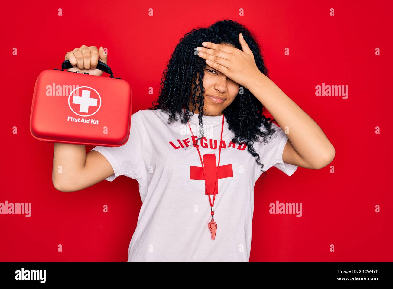 Young african american curly lifeguard woman wearing whistle holding first  aid kit stressed with hand on head, shocked with shame and surprise face, a  Stock Photo - Alamy