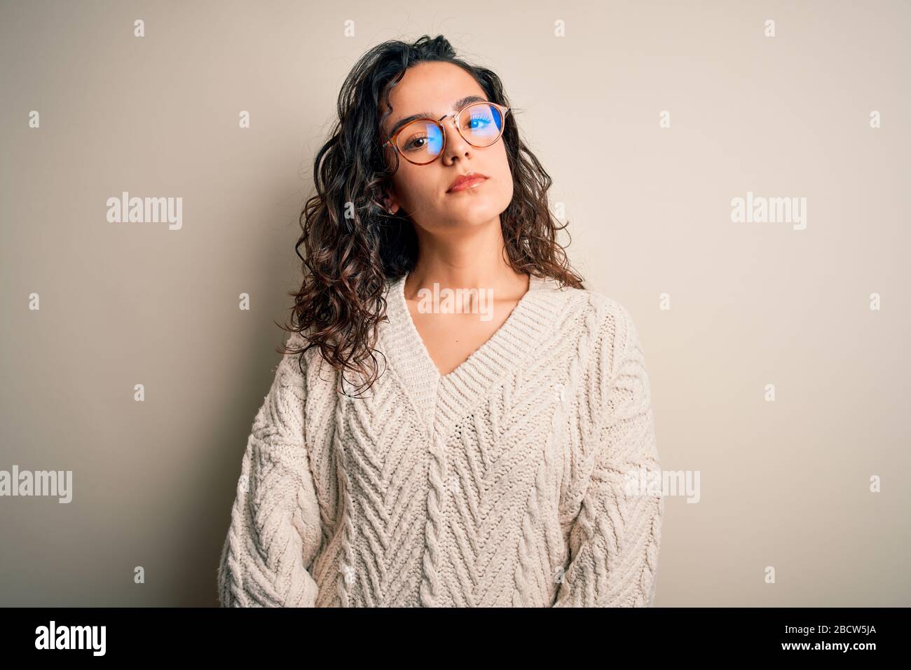 Beautiful woman with curly hair wearing casual sweater and glasses over ...