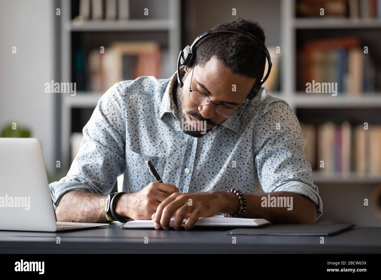 Focused biracial man in headphones make notes studying Stock Photo