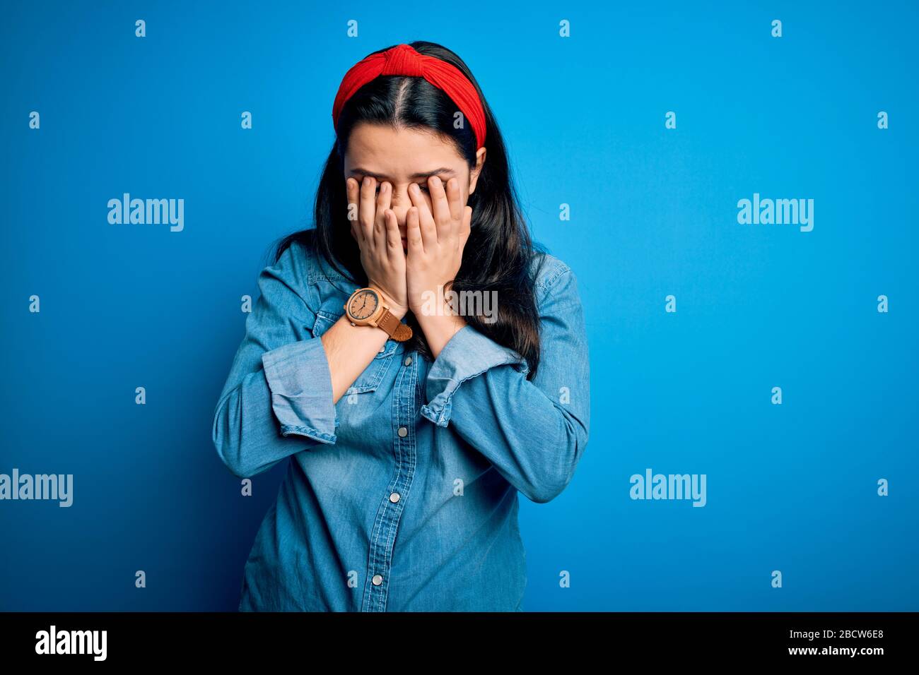 Young brunette woman wearing casual denim shirt over blue isolated background rubbing eyes for fatigue and headache, sleepy and tired expression. Visi Stock Photo