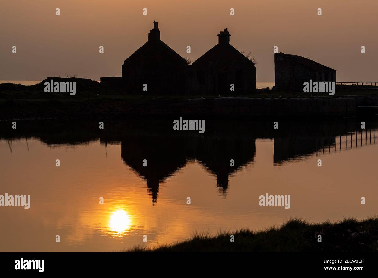 Reflections of Sunset and Silhouetted Buildings in calm water Stock Photo