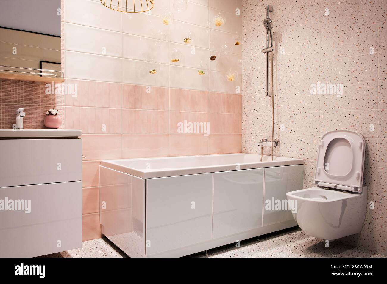 White and pink tones modern bathroom interior with hanging toilet, sink, bath, faucet, mirror, shower, furniture and accessories. Stock Photo