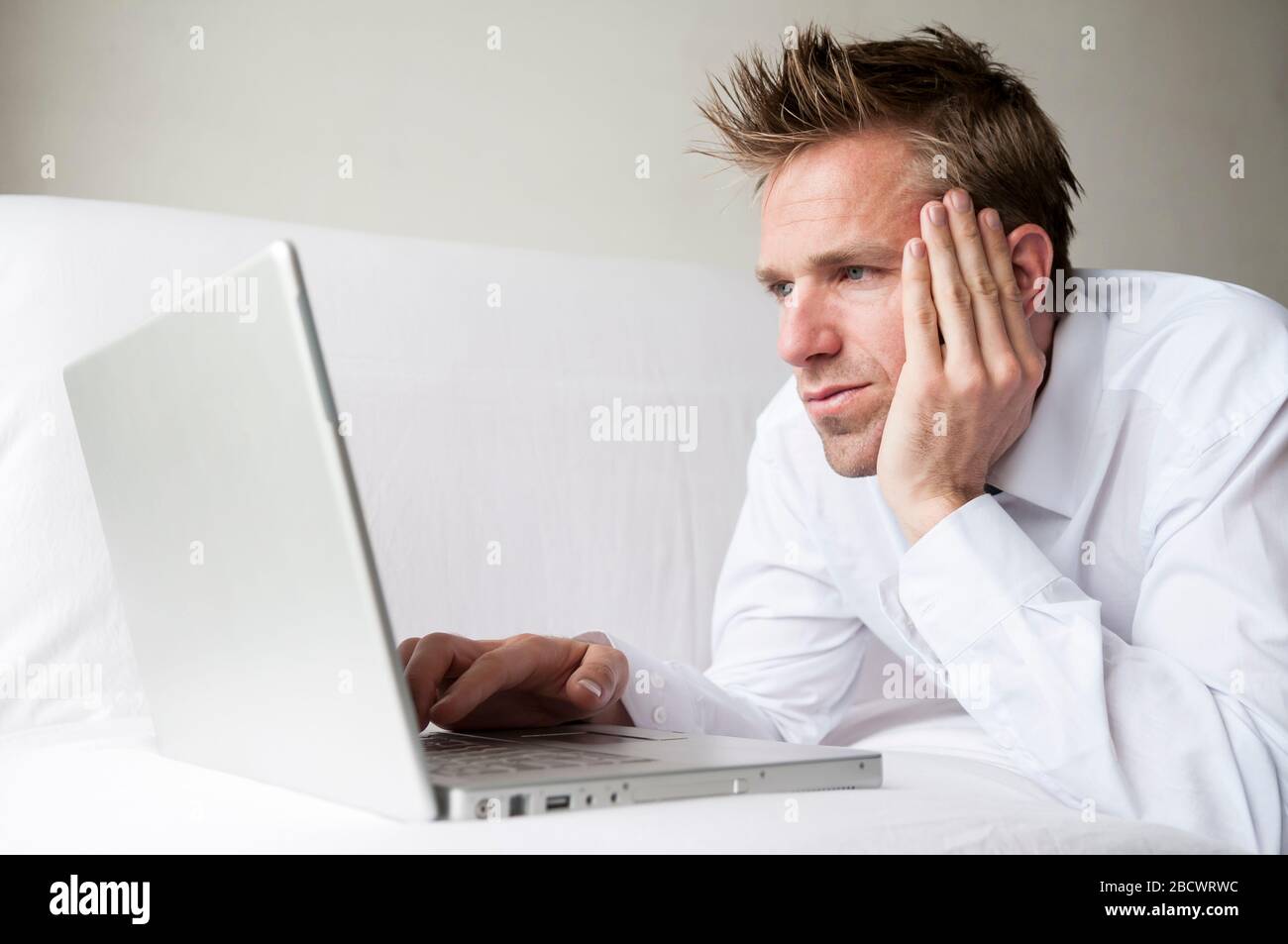 Businessman working remotely lying on white sofa using his laptop computer Stock Photo