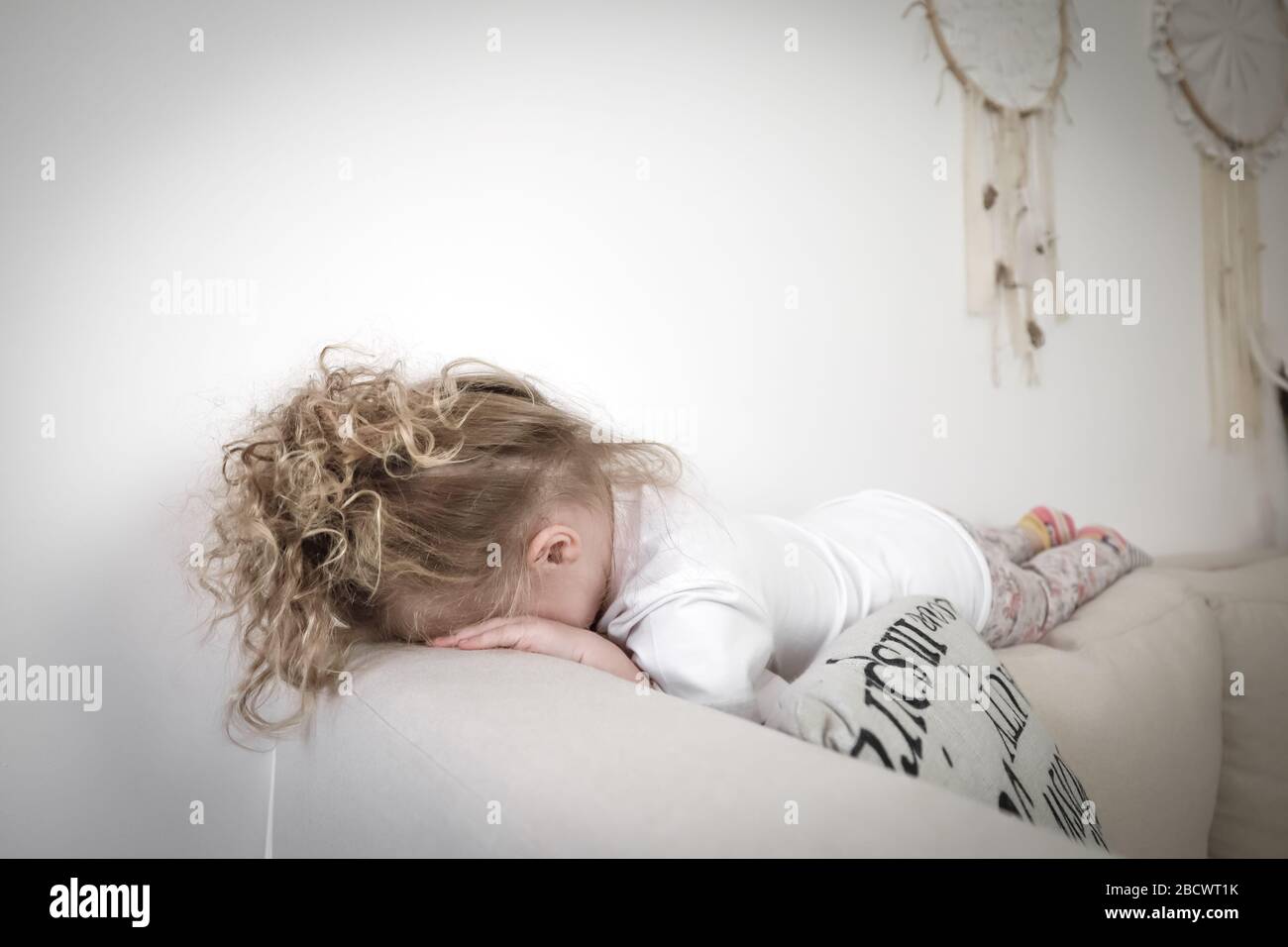 Crying sad toddler girl lies on sofa. Concept of kid grief Stock Photo