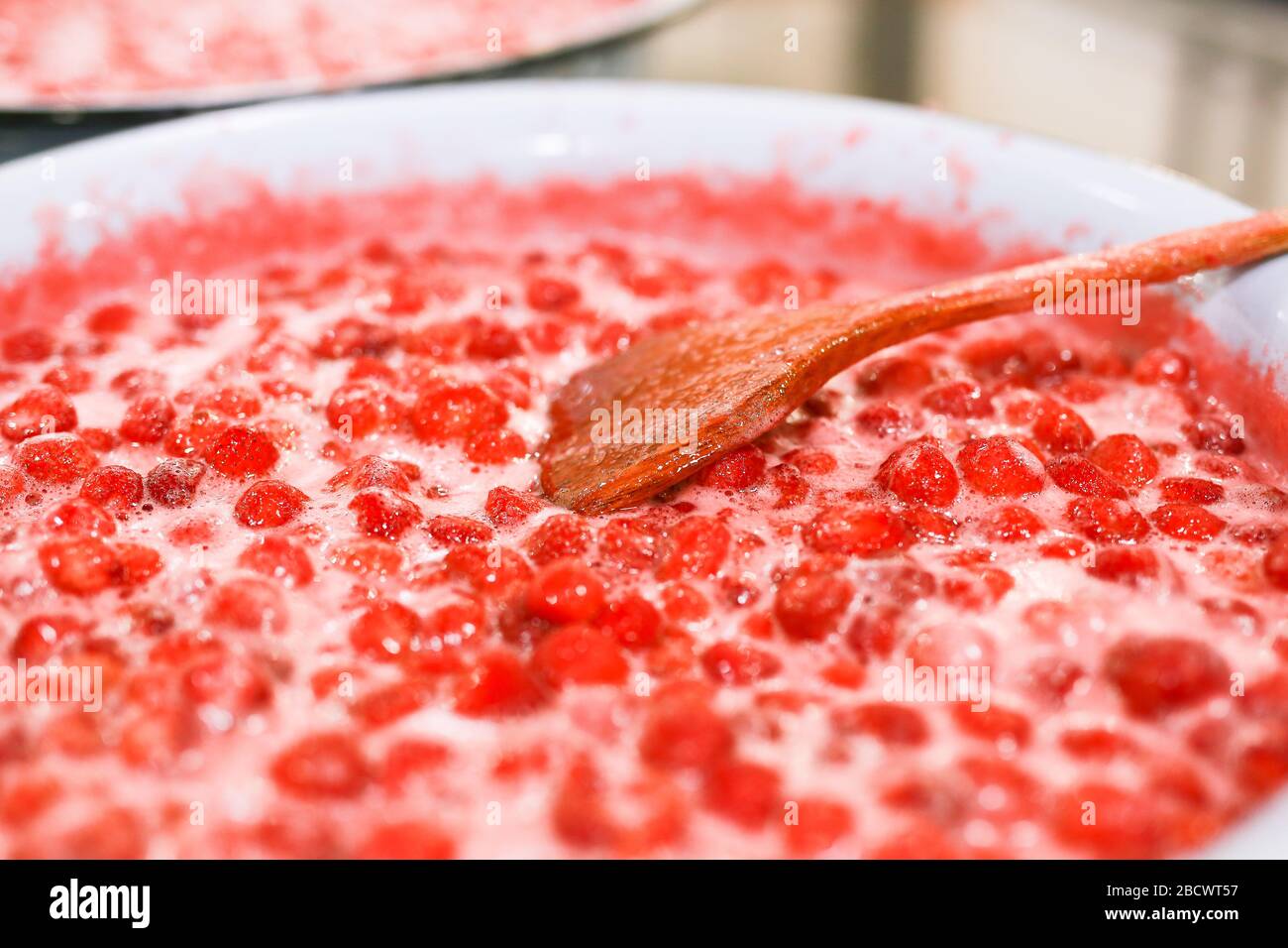 Strawberry jam cooking process. Wooden spoon liying on jam surface