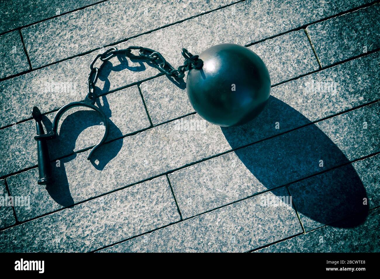 Big black iron ball with chain and shackle casting dramatic shadow outdoors on stone background Stock Photo