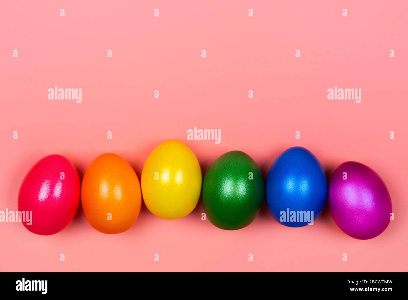 Different colorful eggs in neon trendy colors on coral background. Easter concept. Flat lay