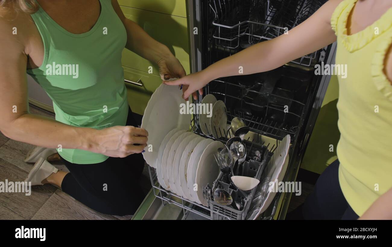 Mother teaching daughter smart girl learning to use dishwasher. Young